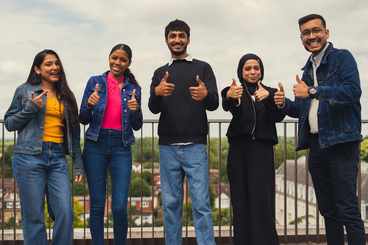 Five students stood on a rooftop all making the thumbs up sign 