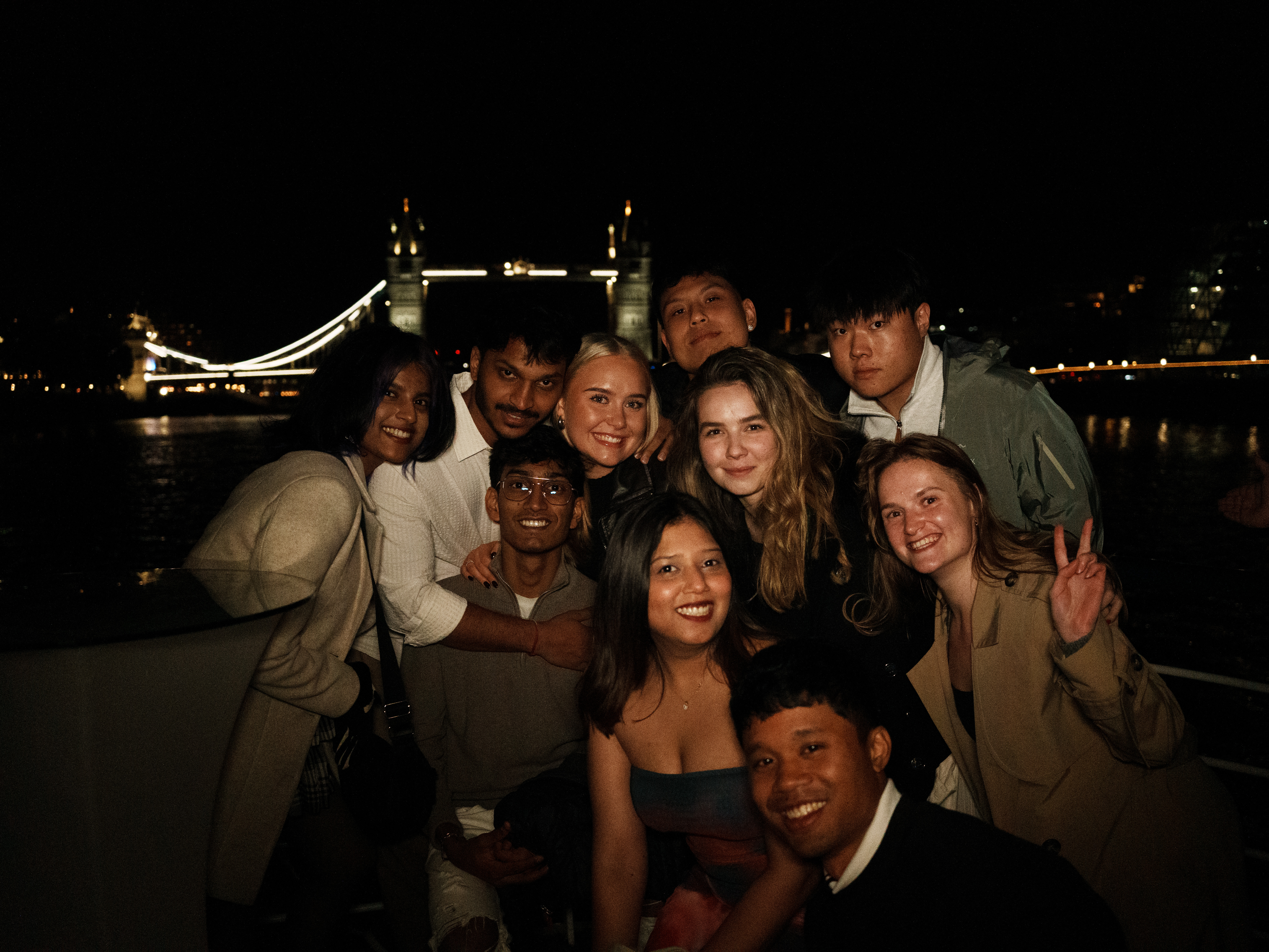 Five students on a boat party posing in front of the Tower Bridge